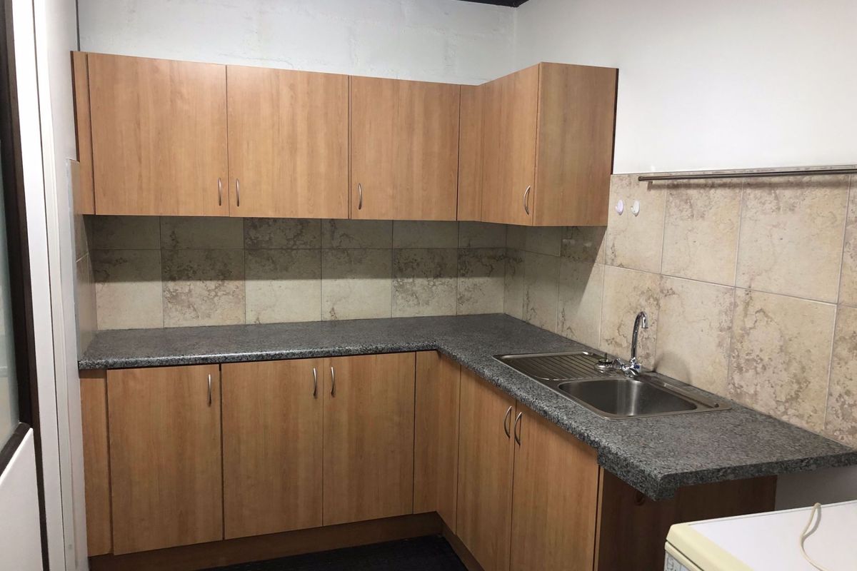A functional kitchen area featuring wood-look laminate cabinetry, granite-effect countertops, a stainless steel sink, and neutral ceramic wall tiling.