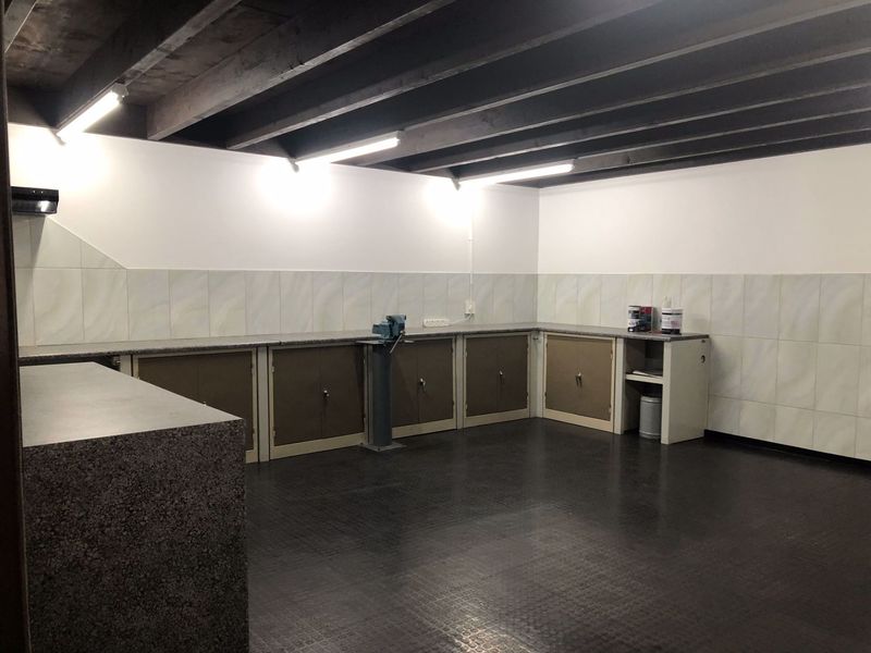 A clean and functional industrial utility space featuring built-in cabinetry, durable rubberized flooring, and exposed timber ceiling beams, suitable for a workshop or storage area.
