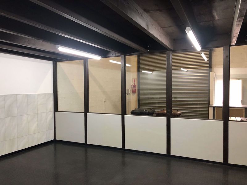 An empty industrial office space featuring exposed timber ceiling beams, glass partitions, and durable vinyl flooring, suitable for a professional workspace.