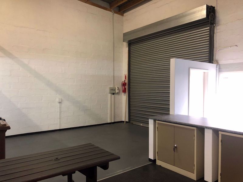 Industrial utility space featuring a large roller shutter door, painted brick walls, and built-in storage cabinetry, suitable for workshop or storage use.