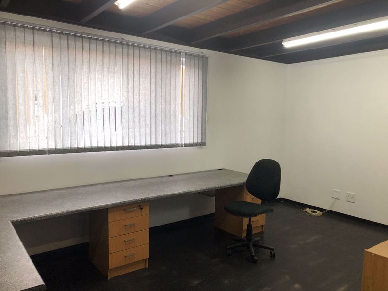 A functional office space featuring a built-in desk, vertical blinds, and exposed ceiling beams, providing a clean and professional work environment.