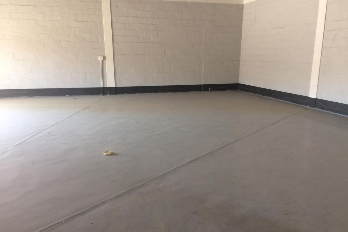 A clean, empty industrial utility space featuring painted brick walls, a smooth concrete floor, and exposed electrical conduit.