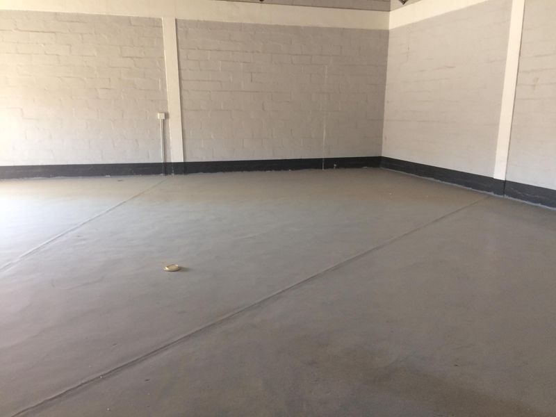 A clean, empty industrial utility space featuring painted brick walls, a smooth concrete floor, and exposed electrical conduit.