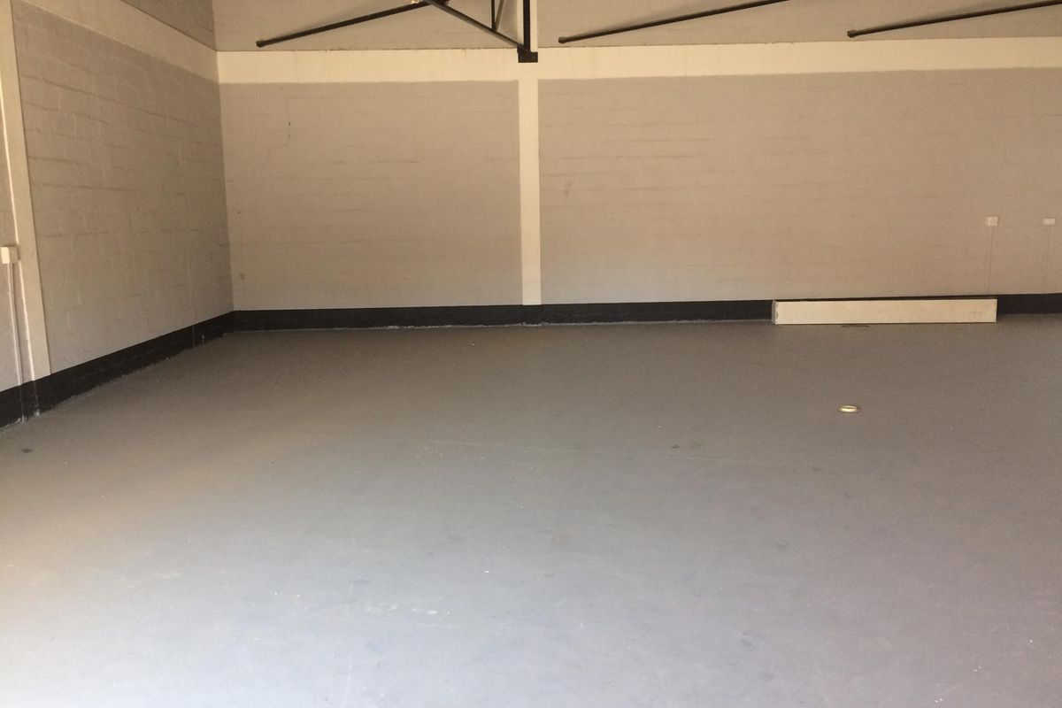 A spacious, empty industrial utility area featuring painted concrete block walls, a smooth concrete floor, and exposed steel roof trusses.