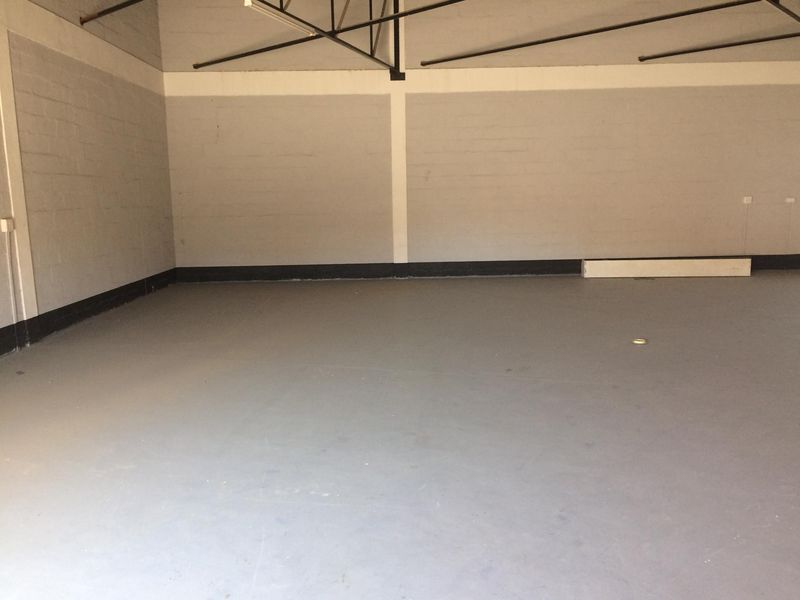 A spacious, empty industrial utility area featuring painted concrete block walls, a smooth concrete floor, and exposed steel roof trusses.