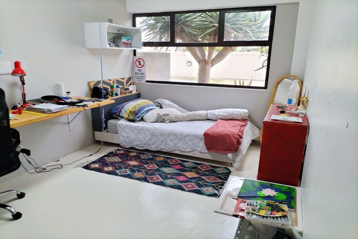 A functional bedroom featuring a built-in desk, large window providing natural light, and smooth painted flooring.