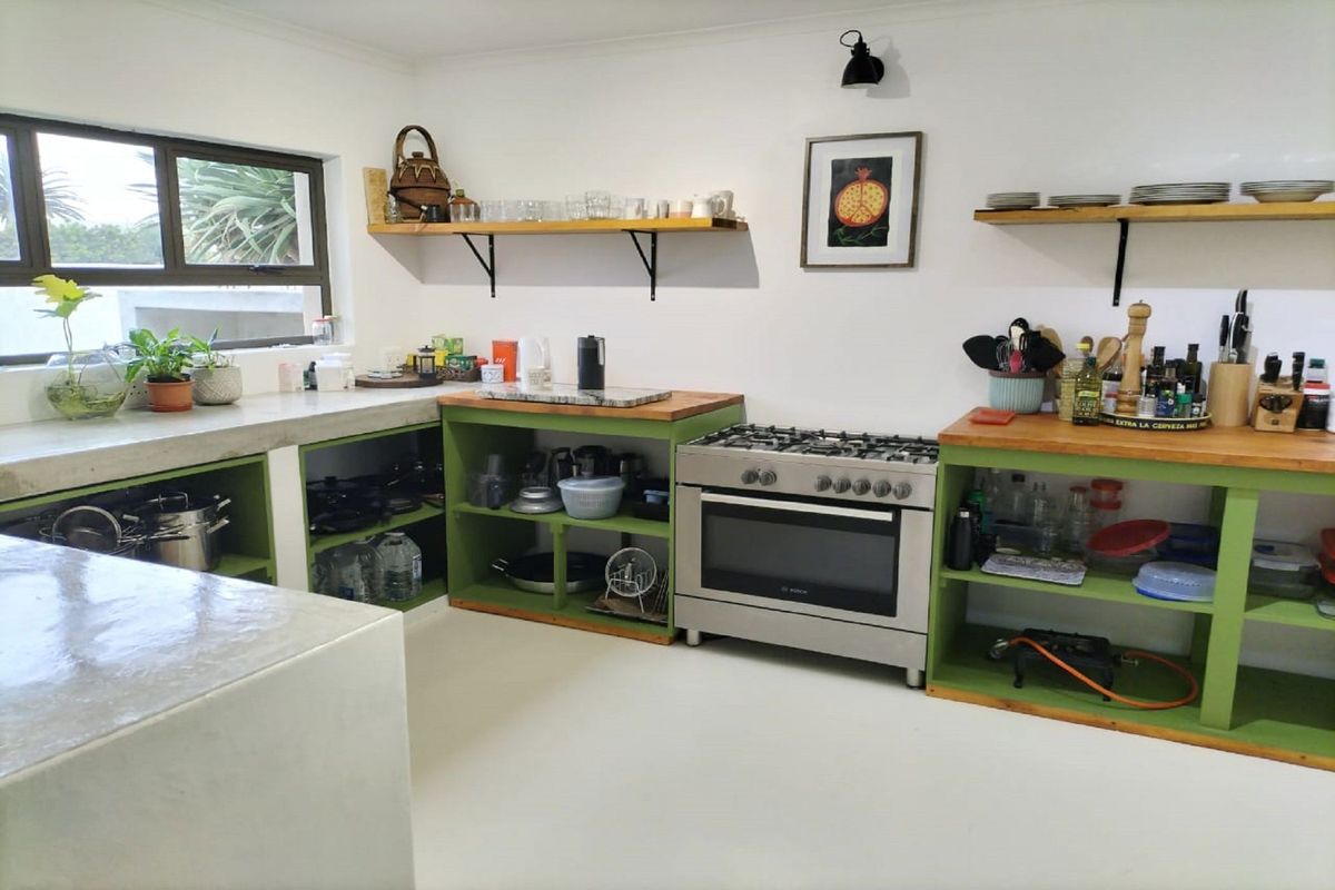 A bright kitchen featuring concrete countertops, timber worktops, open shelving, and a stainless steel gas stove.