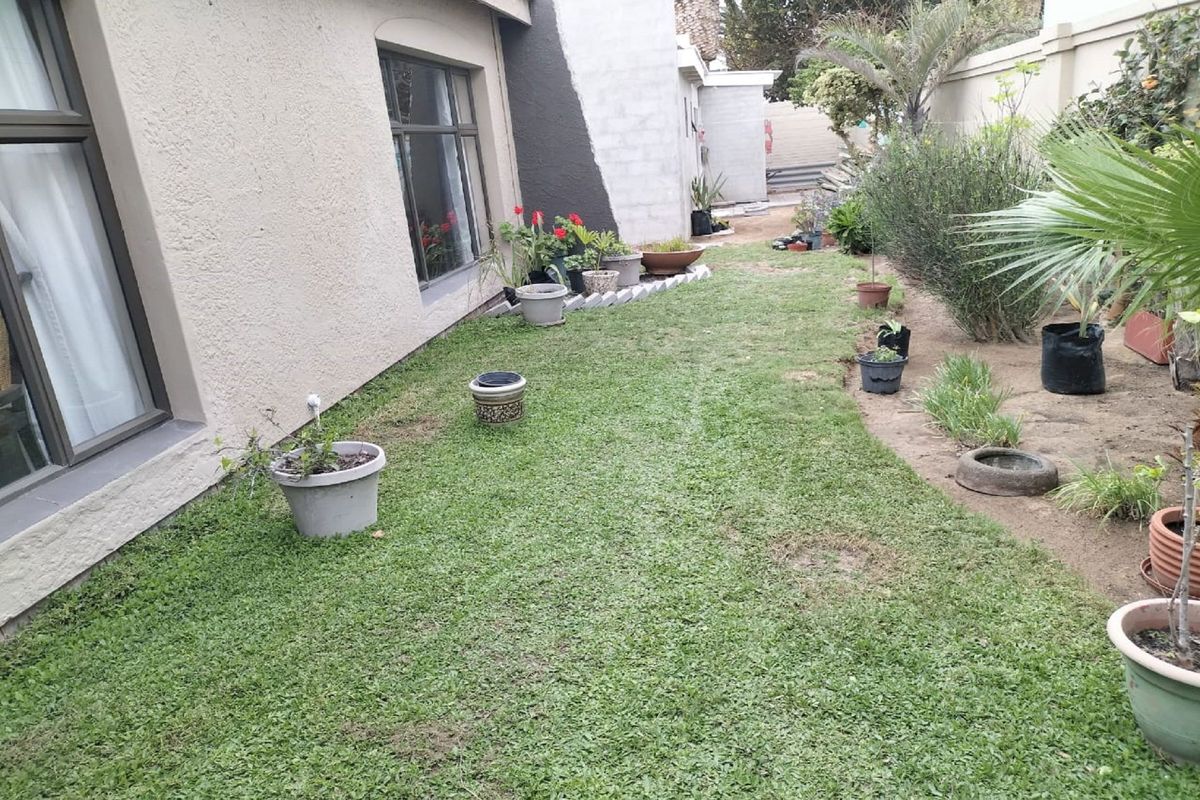 A rear garden area featuring a lawn, boundary wall, and unfinished exterior wall plastering, offering potential for landscaping and exterior improvement.