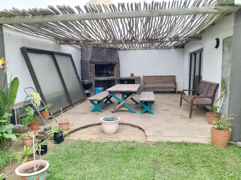 Covered outdoor patio area featuring a built-in braai, tiled flooring, and a rustic pergola roof, providing a functional space for outdoor entertaining.