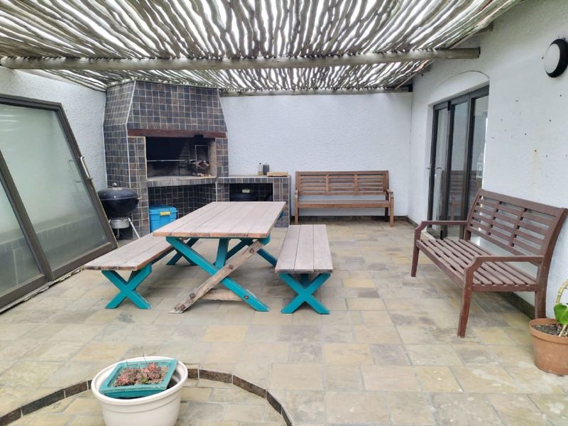 Covered outdoor patio area featuring a built-in braai, tiled flooring, and a rustic pergola roof, providing a functional space for outdoor entertaining.