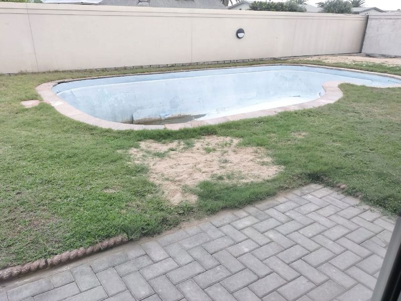 Outdoor pool area featuring a paved patio, boundary wall, and an empty swimming pool requiring maintenance and landscaping.