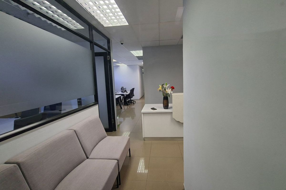 A professional office reception area featuring tiled flooring, a built-in reception desk, and glass-partitioned office spaces with suspended ceilings.