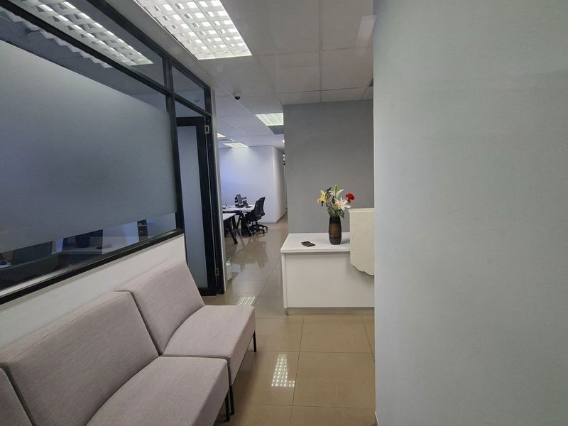 A professional office reception area featuring tiled flooring, a built-in reception desk, and glass-partitioned office spaces with suspended ceilings.