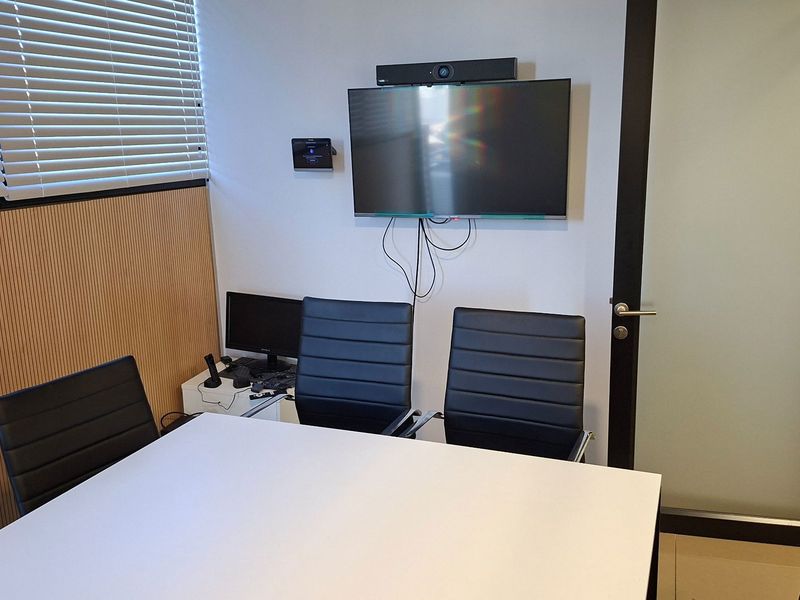A functional office meeting room featuring slatted wood wall paneling, venetian blinds, and a wall-mounted display screen with a frosted glass entry door.
