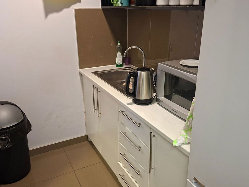 A compact scullery or kitchenette area featuring built-in white cabinetry, a stainless steel sink, and tiled splashback finishes.