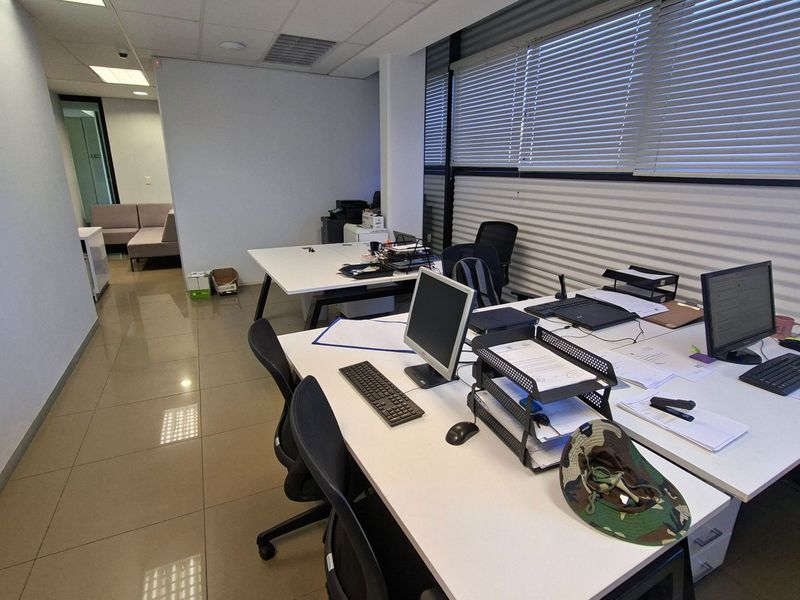 A functional office space featuring tiled flooring, suspended ceilings with recessed lighting, and large windows equipped with venetian blinds.