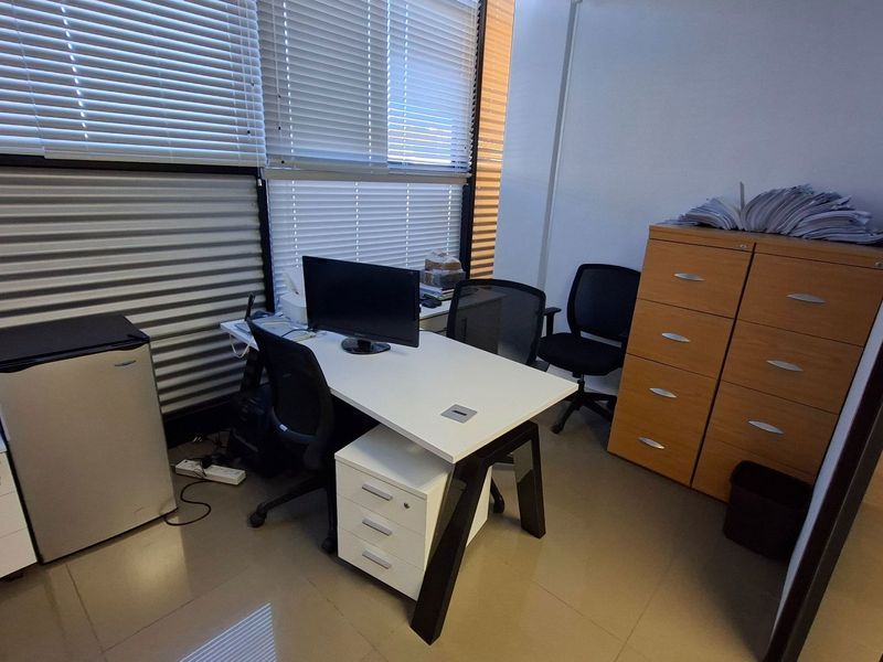 A functional office space featuring tiled flooring, large windows with venetian blinds, and built-in storage cabinetry.
