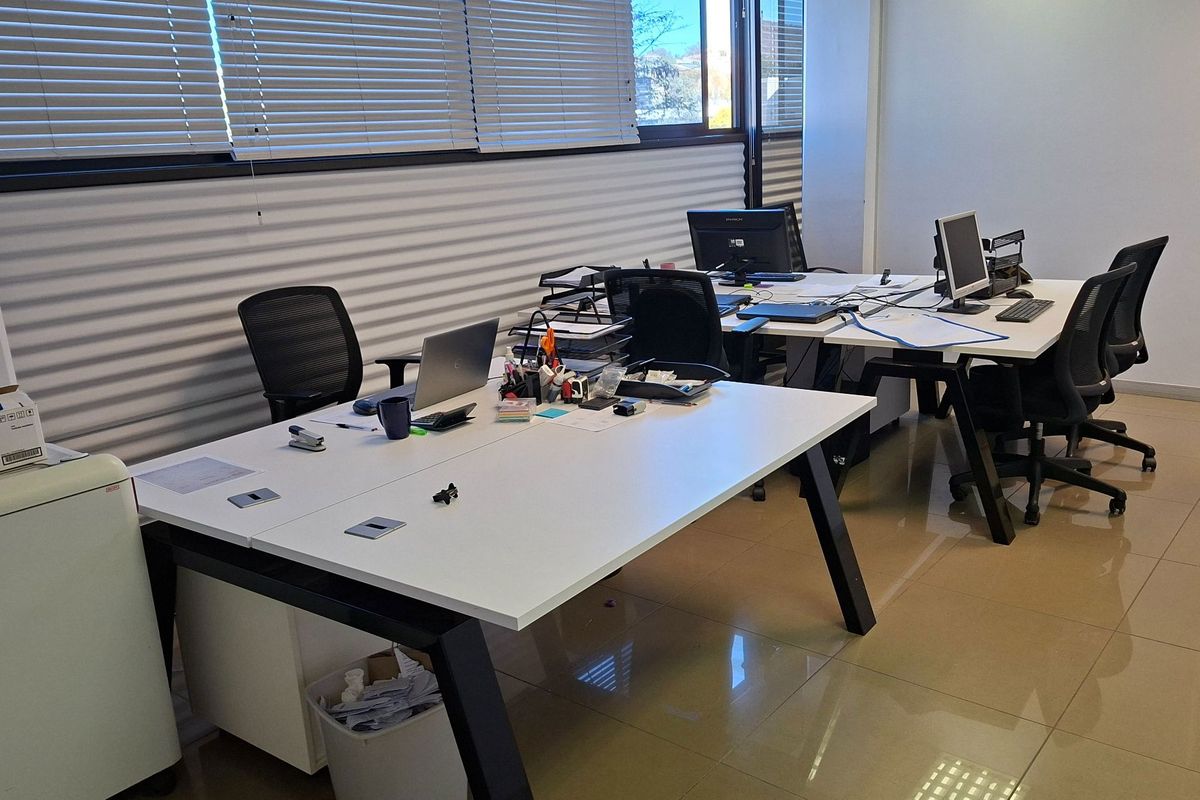 A functional office space featuring tiled flooring and large windows with adjustable venetian blinds, providing a bright and professional work environment.