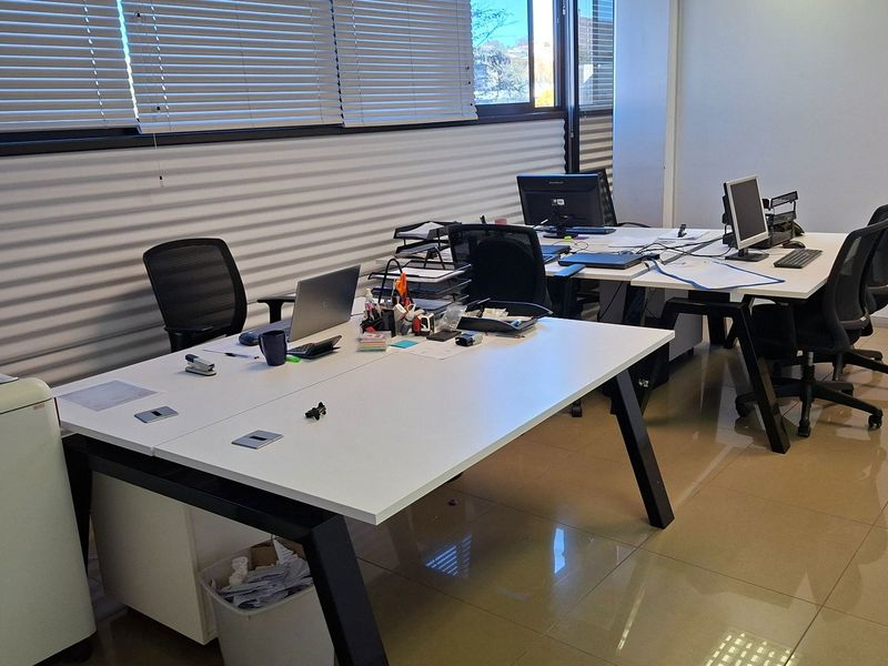 A functional office space featuring tiled flooring and large windows with adjustable venetian blinds, providing a bright and professional work environment.