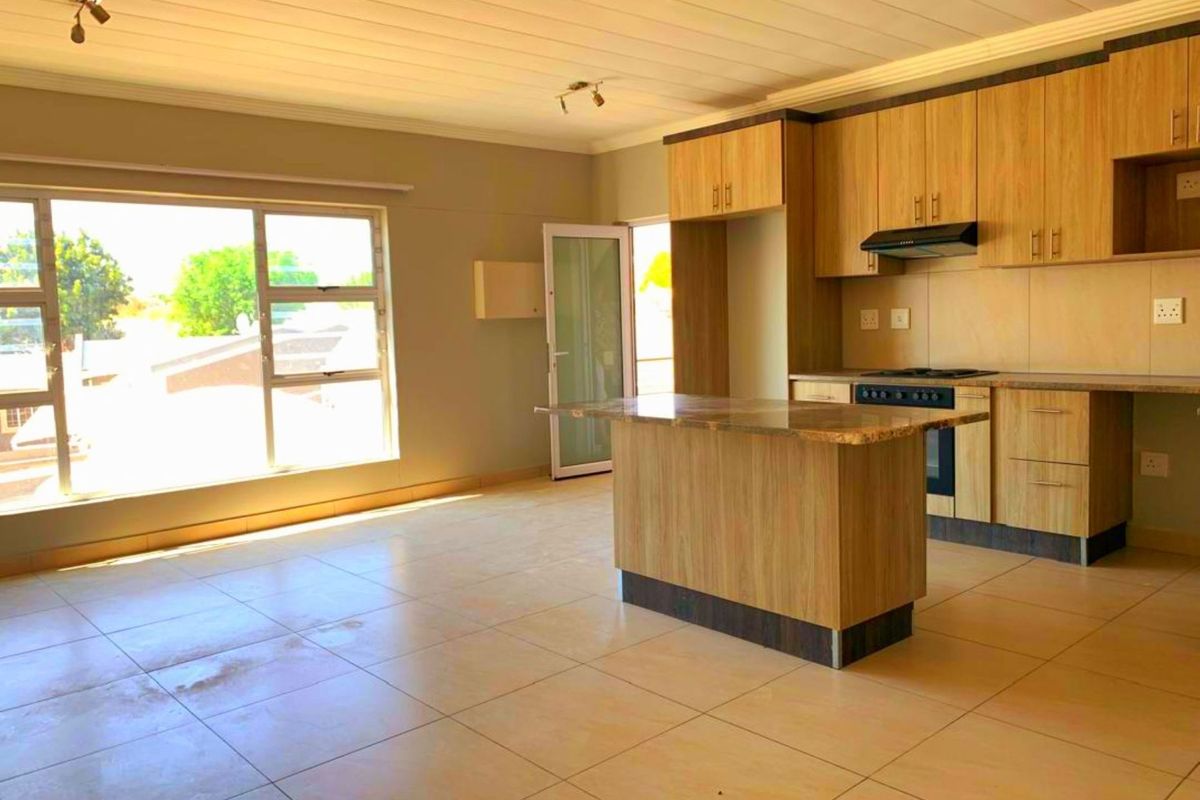 Spacious open-plan living and kitchen area featuring light wood cabinetry, a central island, built-in oven, and large windows providing ample natural light.
