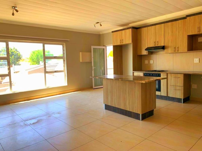 Spacious open-plan living and kitchen area featuring light wood cabinetry, a central island, built-in oven, and large windows providing ample natural light.