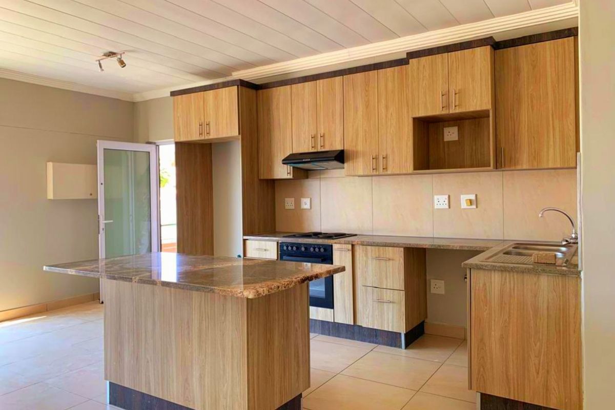 Modern kitchen featuring wood-finish cabinetry, granite countertops, a central island, built-in oven, hob, and extractor fan, with tiled flooring throughout.