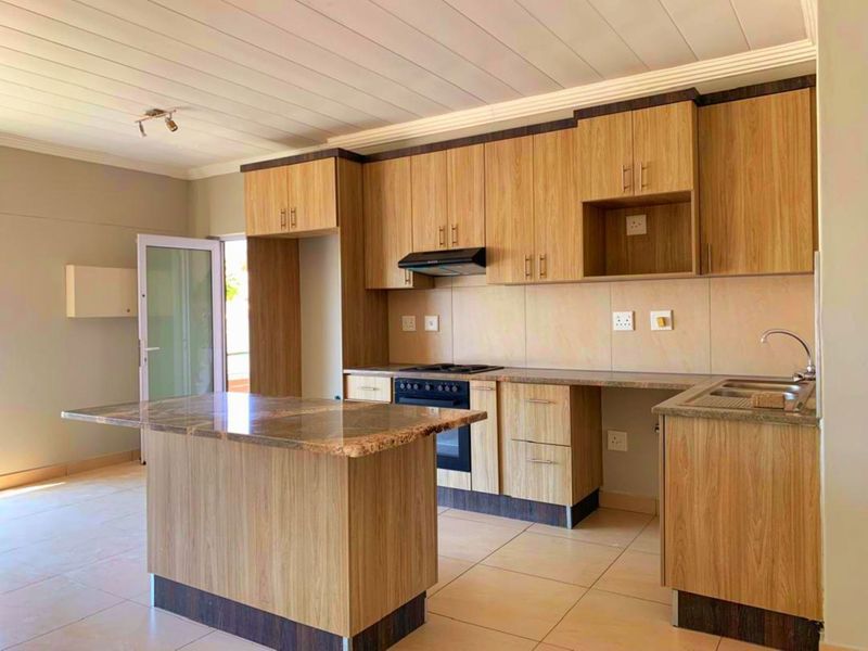 Modern kitchen featuring wood-finish cabinetry, granite countertops, a central island, built-in oven, hob, and extractor fan, with tiled flooring throughout.