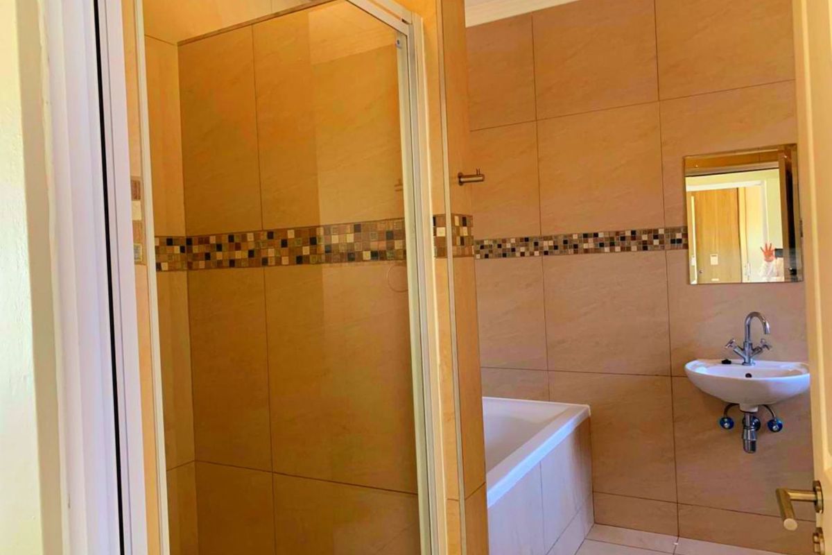 A functional bathroom featuring a shower enclosure, bathtub, pedestal sink, and neutral wall tiling with a decorative mosaic accent border.