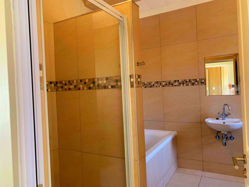 A functional bathroom featuring a shower enclosure, bathtub, pedestal sink, and neutral wall tiling with a decorative mosaic accent border.