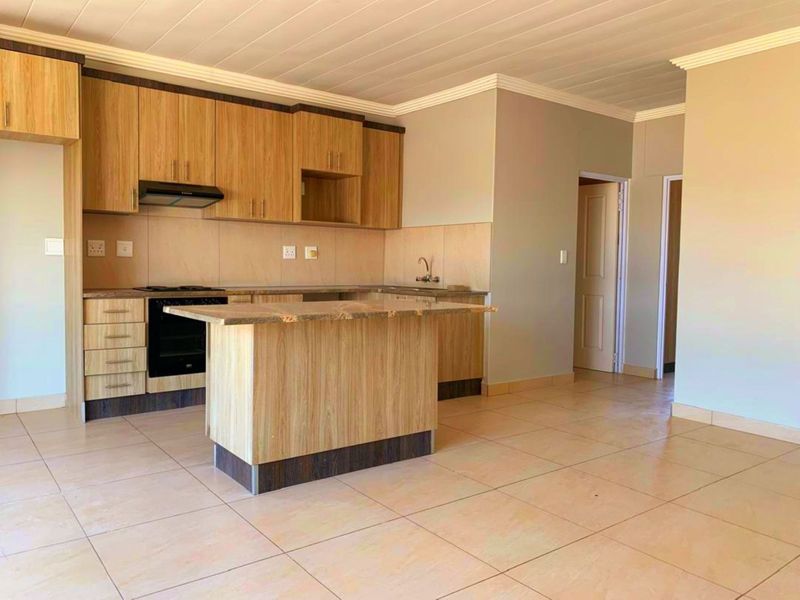 Modern kitchen featuring light wood cabinetry, granite countertops, a central island, and integrated appliances, set within an open-plan living space with tiled flooring.