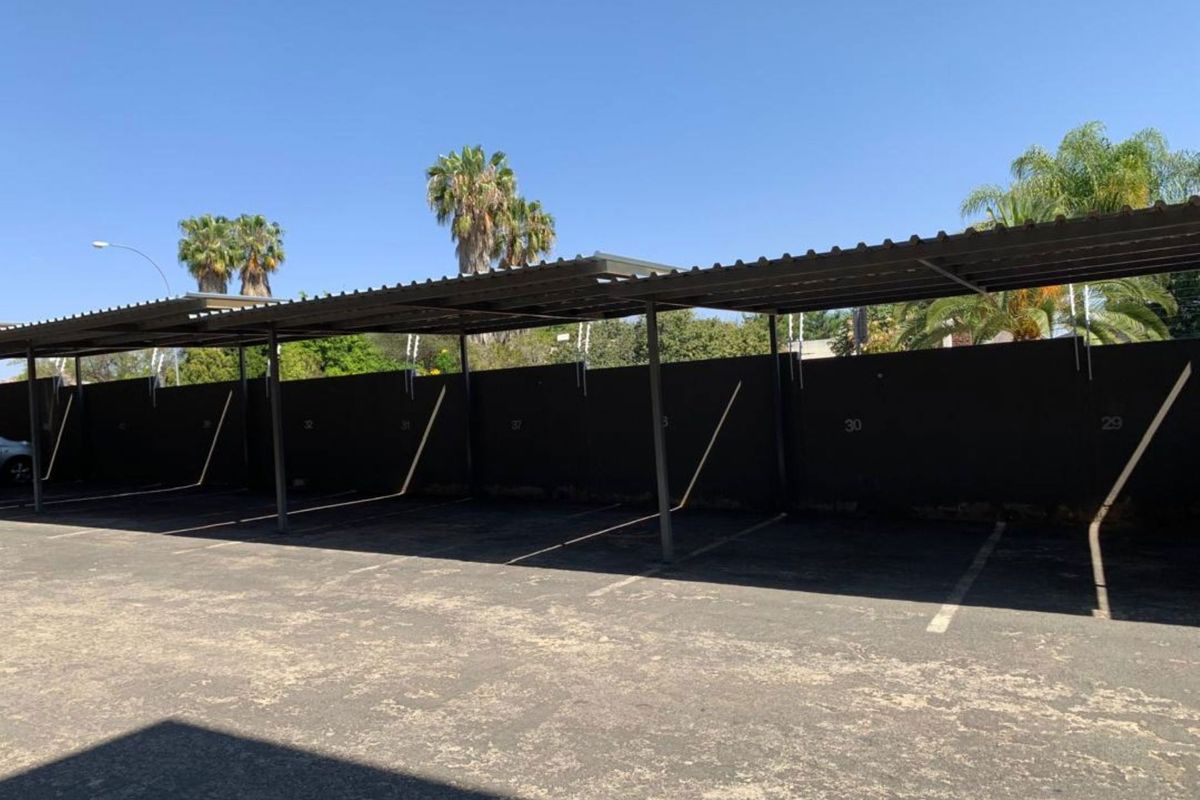 A row of covered parking bays featuring a metal roof structure and asphalt paving within a secure complex.