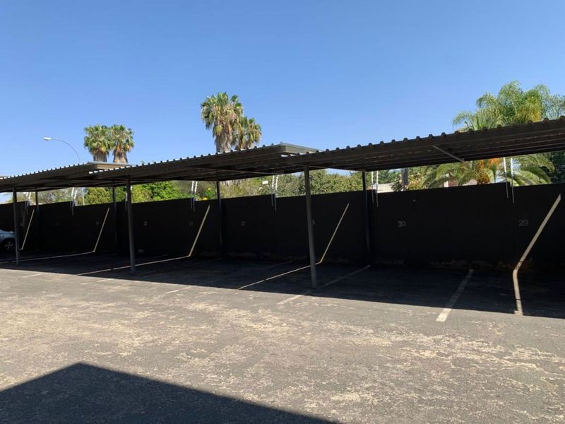 A row of covered parking bays featuring a metal roof structure and asphalt paving within a secure complex.