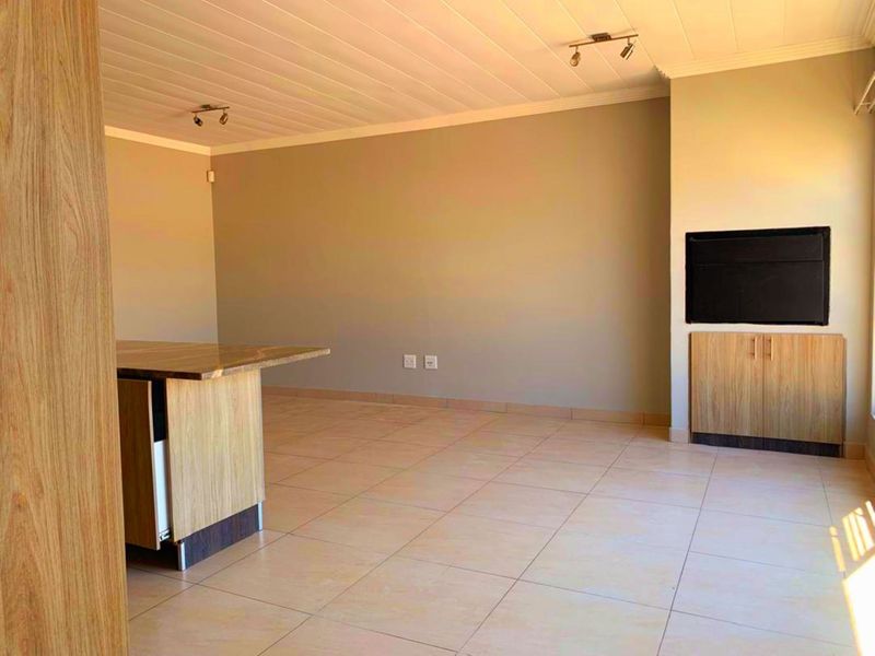 Spacious open-plan living area featuring tiled flooring, a kitchen island, and built-in cabinetry, offering a versatile layout for modern apartment living.
