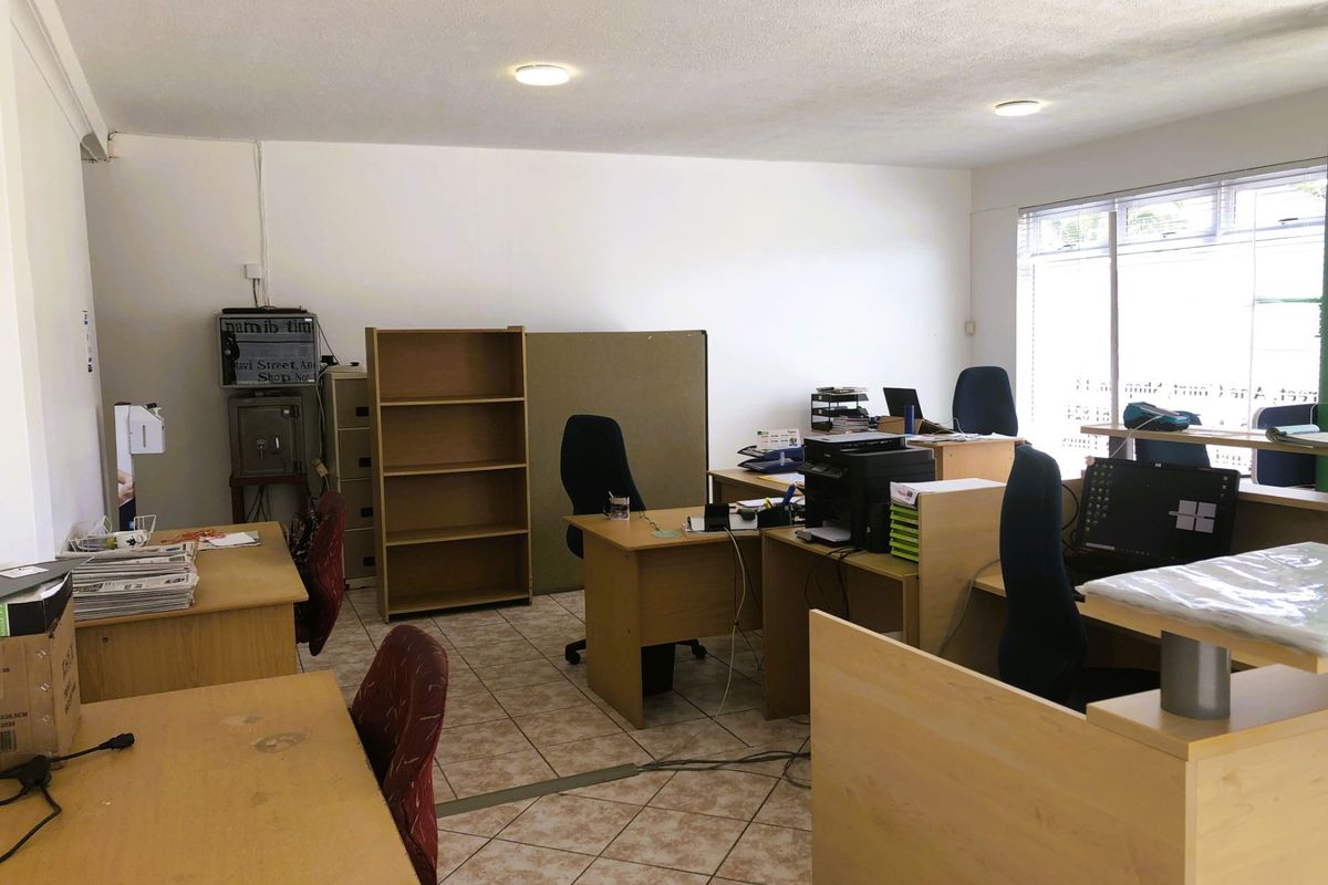 A functional office space featuring tiled flooring, recessed ceiling lighting, and large windows providing natural light.