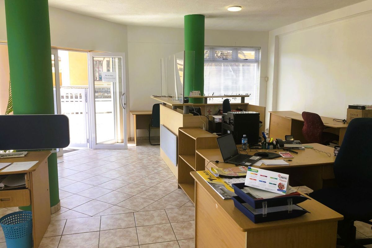Open-plan office space featuring tiled flooring, structural columns, and a built-in reception desk with a glass partition.