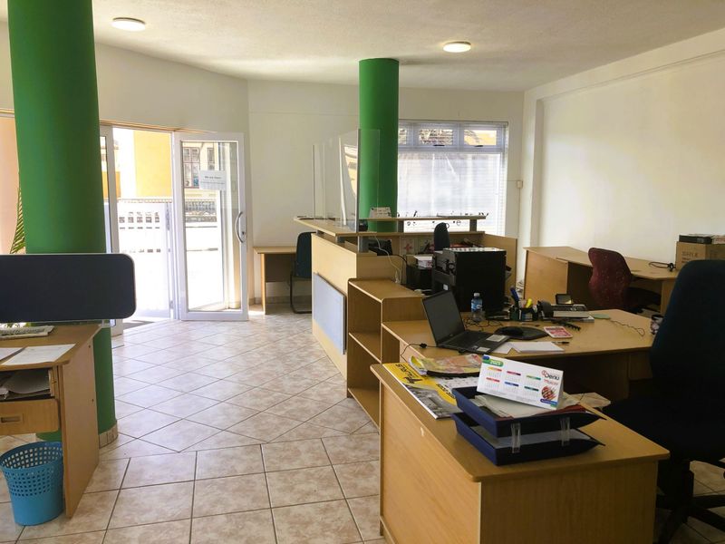 Open-plan office space featuring tiled flooring, structural columns, and a built-in reception desk with a glass partition.