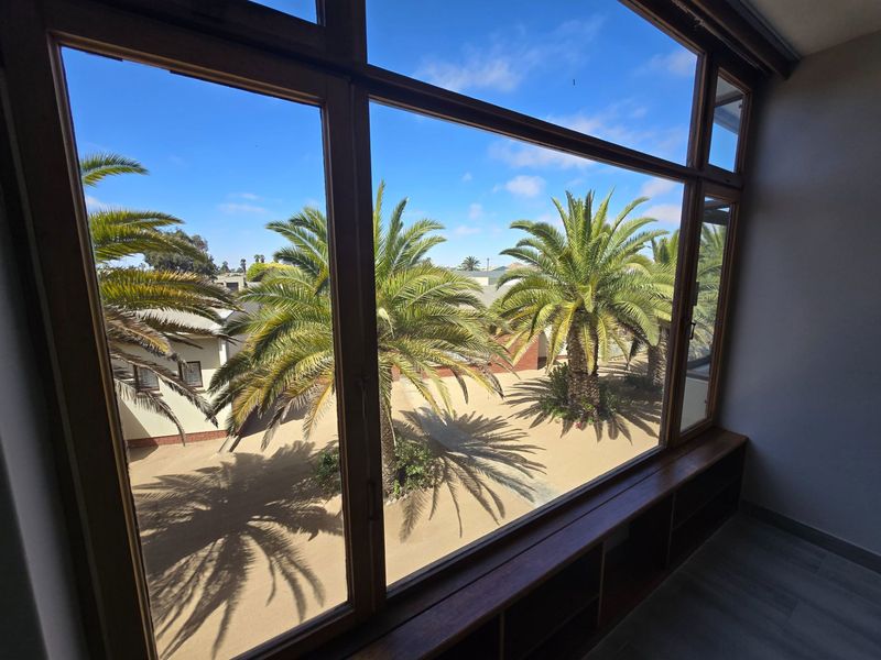 A bright interior space featuring large timber-framed windows that offer a clear view of the landscaped courtyard with palm trees.