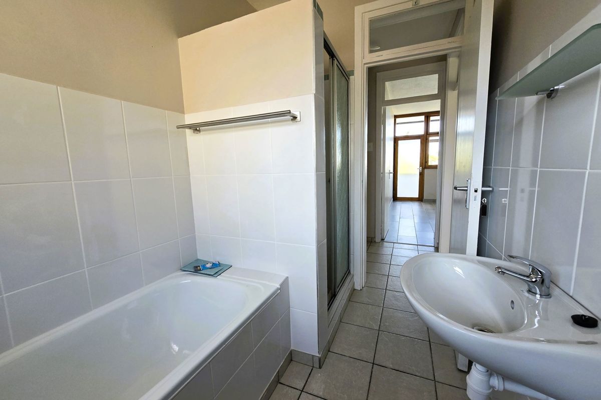 A functional bathroom featuring a bathtub, separate shower enclosure, and pedestal washbasin with neutral wall and floor tiling.
