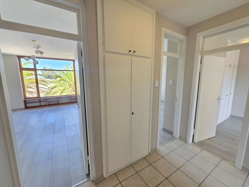 A bright, tiled hallway featuring built-in storage cupboards and access to adjacent rooms with large windows providing natural light.
