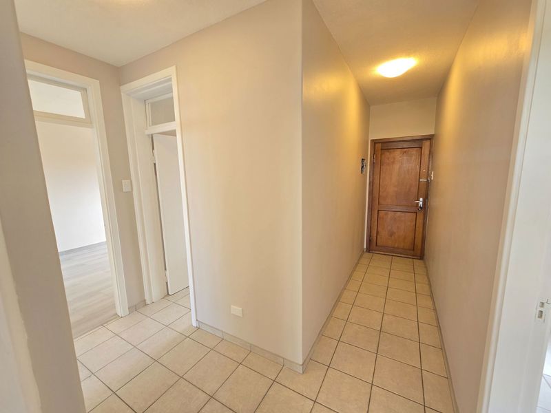 A clean, neutral-toned entrance hallway featuring tiled flooring, a solid wood front door, and access to adjacent rooms through classic door frames.