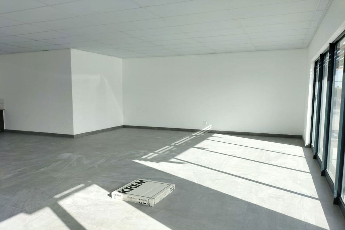 A bright, open-plan retail space featuring modern tiled flooring, a suspended ceiling, and large glass sliding doors providing ample natural light.