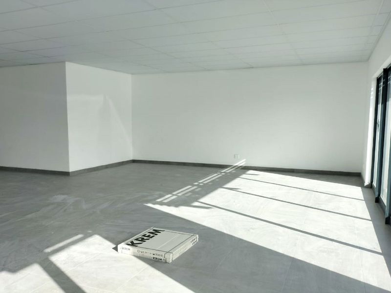 A bright, open-plan retail space featuring modern tiled flooring, a suspended ceiling, and large glass sliding doors providing ample natural light.