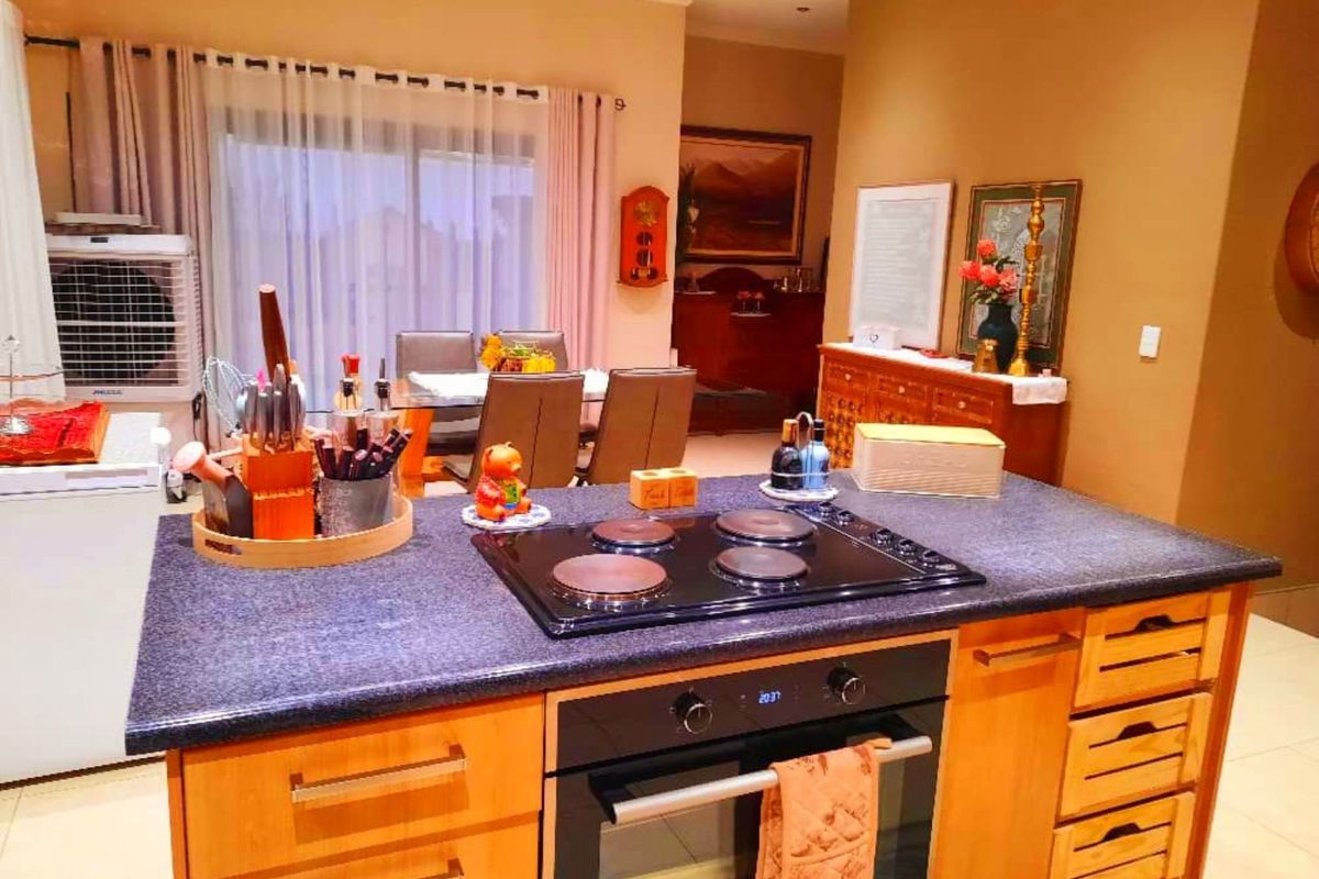 A functional kitchen featuring a central island with a built-in oven and electric cooktop, complemented by wooden cabinetry and tiled flooring.