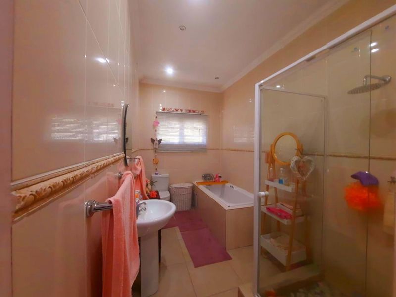 A functional bathroom featuring a pedestal basin, built-in bathtub, and a separate glass-enclosed shower with neutral wall and floor tiling.