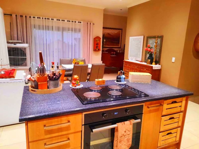 A functional kitchen featuring a central island with a built-in oven and electric cooktop, complemented by wooden cabinetry and tiled flooring.