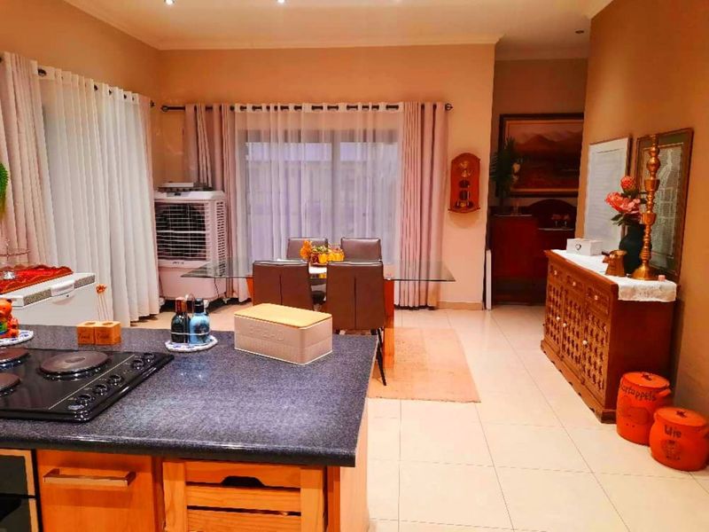 Open-plan kitchen and dining area featuring granite countertops, a built-in hob, tiled flooring, and sliding glass doors leading to the exterior.
