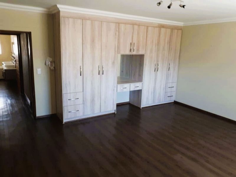 Spacious bedroom featuring extensive light wood-finish built-in cupboards with integrated vanity and dark laminate flooring.