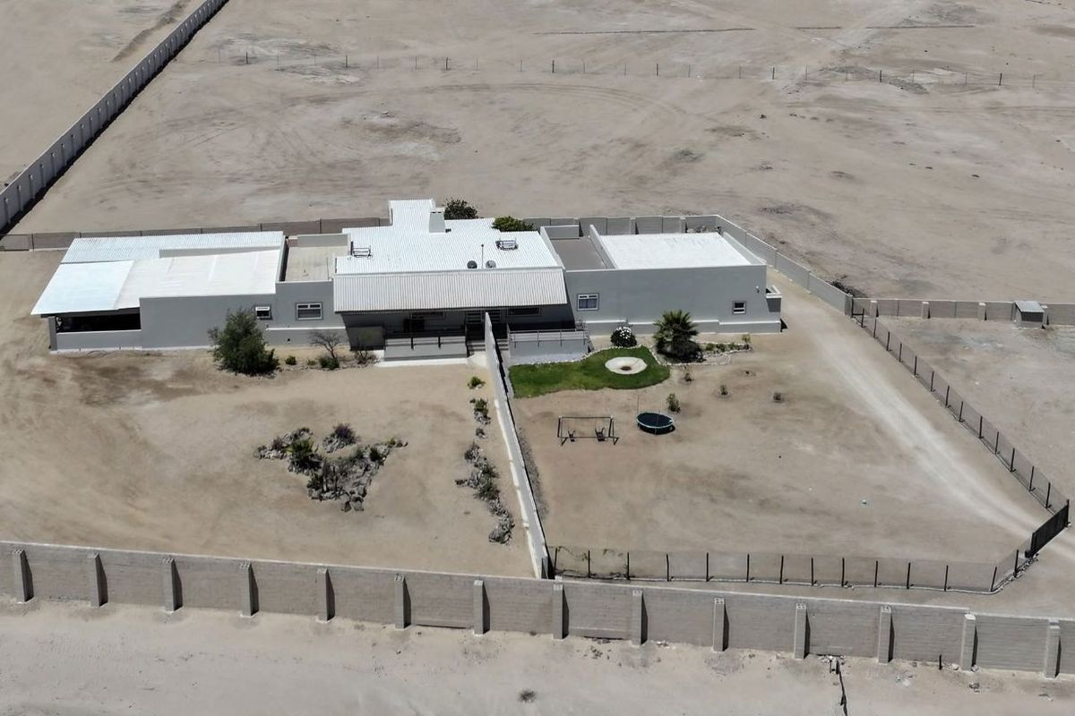 Aerial view of a single-story farmhouse property situated on a large, fenced plot of land in a desert landscape.
