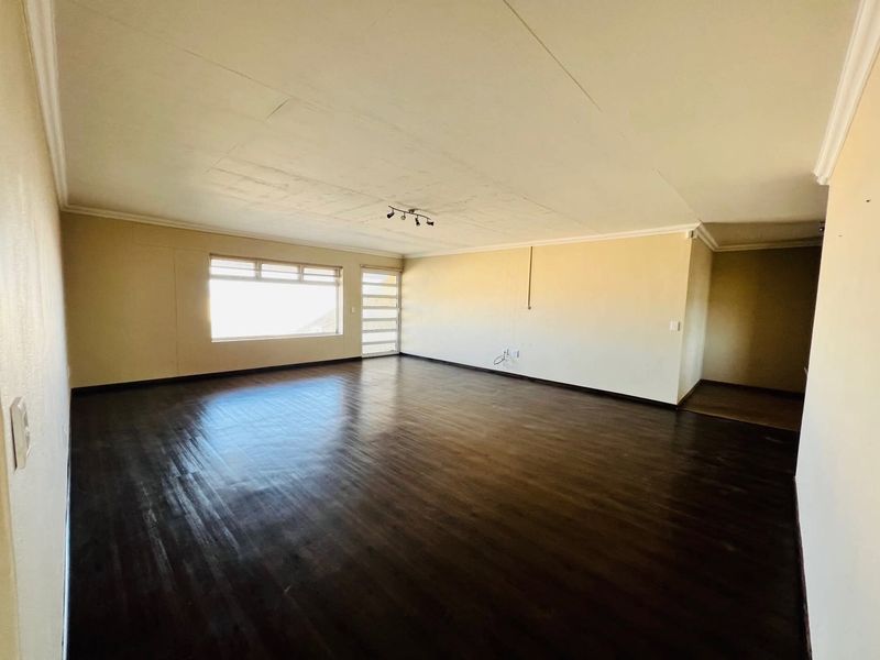 A spacious, empty living area featuring dark laminate flooring, coved ceilings, and natural light from a large window and glass panel door.