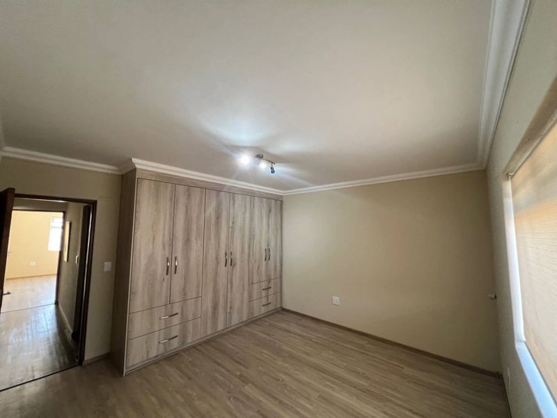 A spacious bedroom featuring modern wood-look laminate flooring, neutral wall tones, and extensive built-in cabinetry for ample storage.